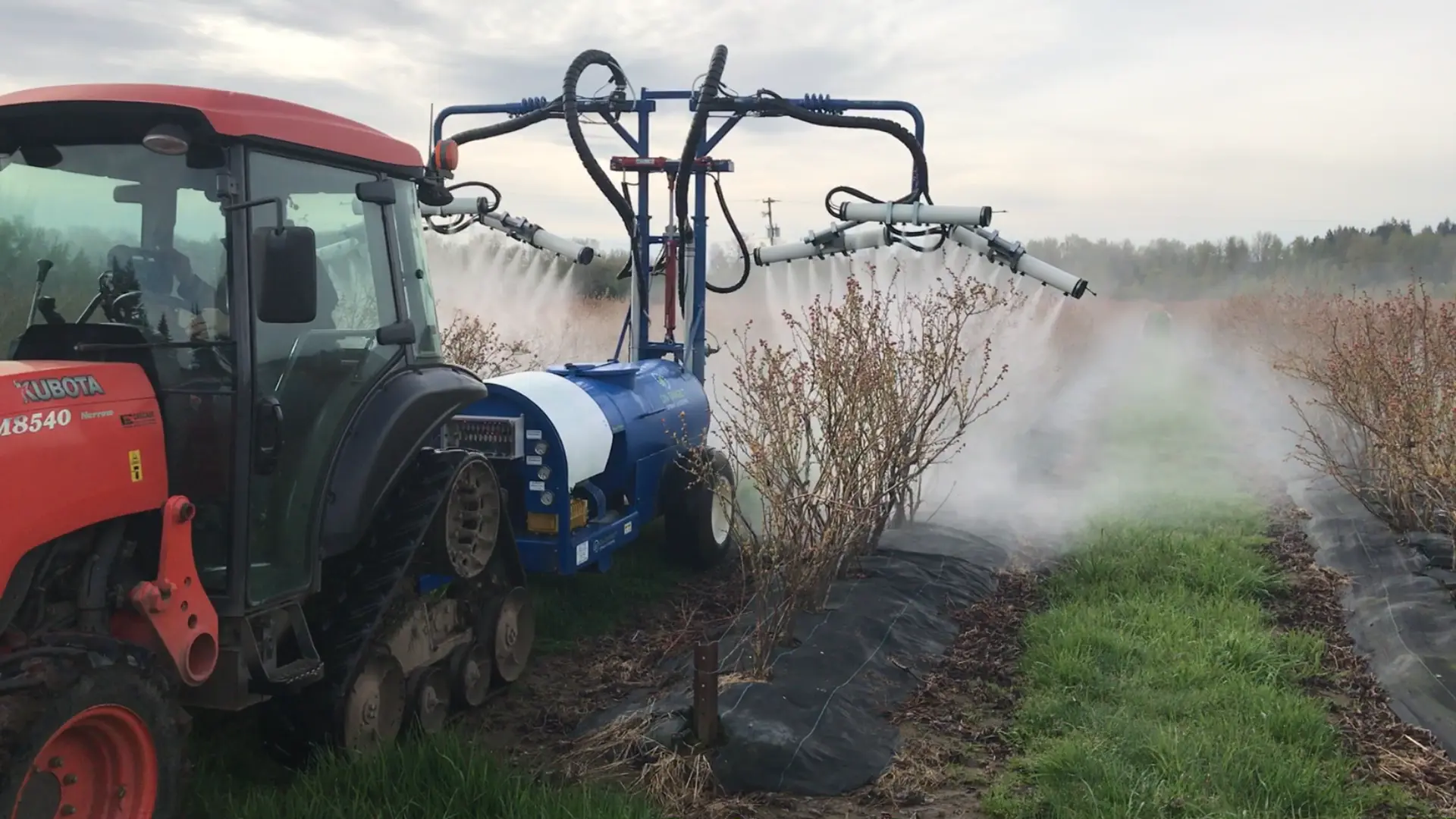 Narrow 200-gallon OnTarget sprayer pulled by a compact tractor through blueberry rows